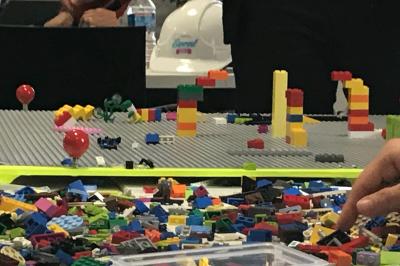 Miniature Lego Furious Play Deux personnes assises dans un buggy bleu en extérieur, discutant et manipulant des objets, avec un homme debout à côté.