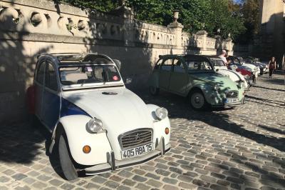 Miniature Rallye 2cv Deux personnes assises dans un buggy bleu en extérieur, discutant et manipulant des objets, avec un homme debout à côté.