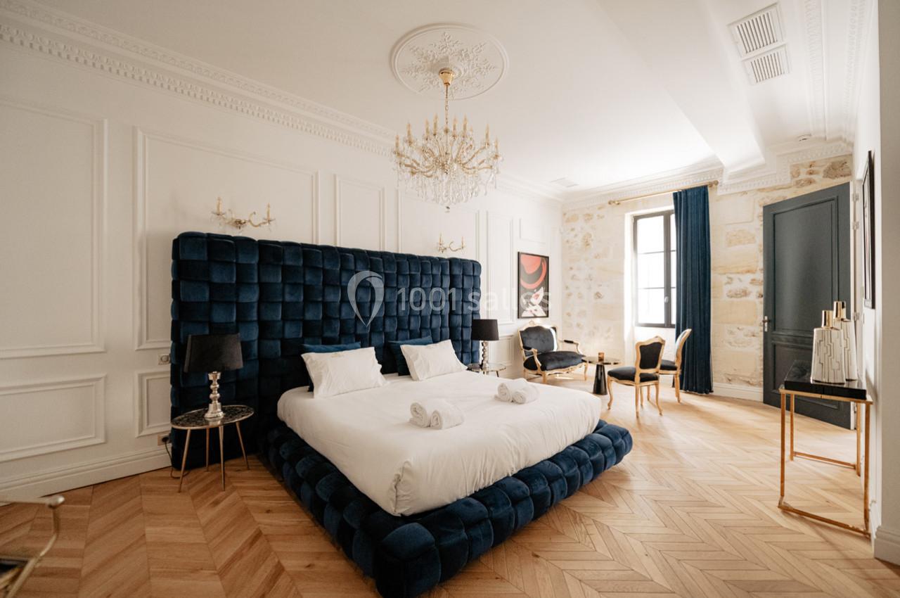 Chambre élégante avec lit à tête de lit capitonnée bleue, parquet en bois clair et décoration classique raffinée.