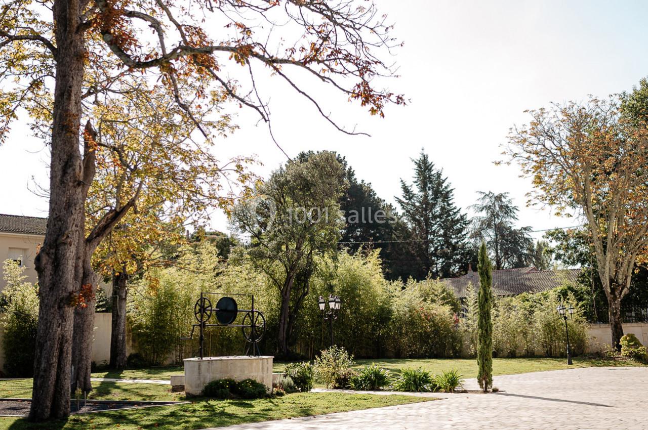 Cour extérieure avec un puits en pierre, des arbres aux feuilles d'automne et un chemin pavé bordé de végétation.
