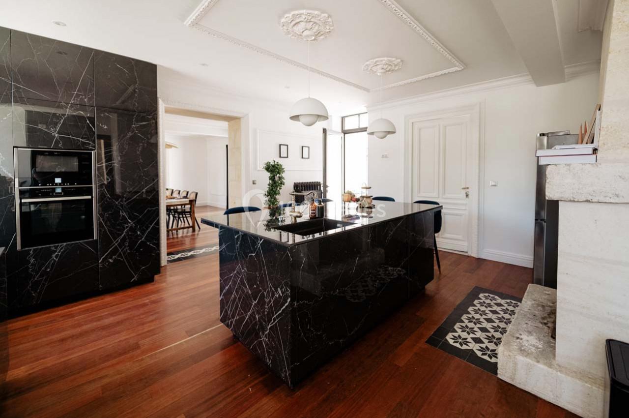 Cuisine moderne avec îlot central en marbre noir, parquet en bois, luminaires suspendus et éléments décoratifs élégants.