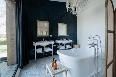 Baignoire blanche près d'une fenêtre, avec deux flacons de savon sur un tabouret en bois dans un espace lumineux.