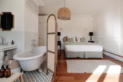 Vue d'une salle de bain avec une baignoire blanche, un tabouret en bois portant deux flacons, et une vitre donnant sur un…