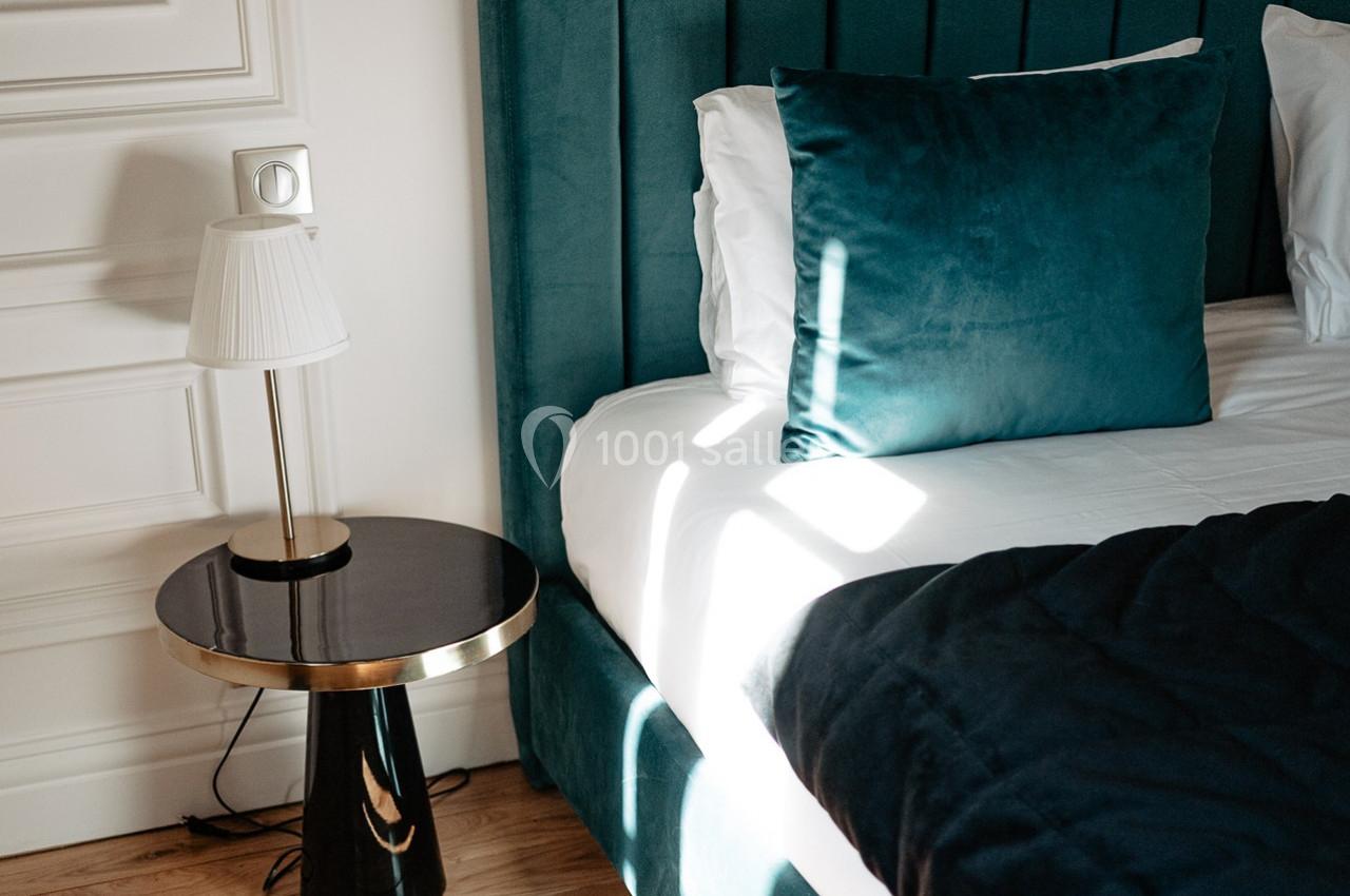 Lit avec tête de lit verte, coussin assorti, table de chevet noire et lampe blanche dans une chambre lumineuse.