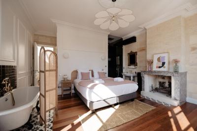 Vue d'une salle de bain avec une baignoire blanche, un tabouret en bois portant deux flacons, et une vitre donnant sur un…