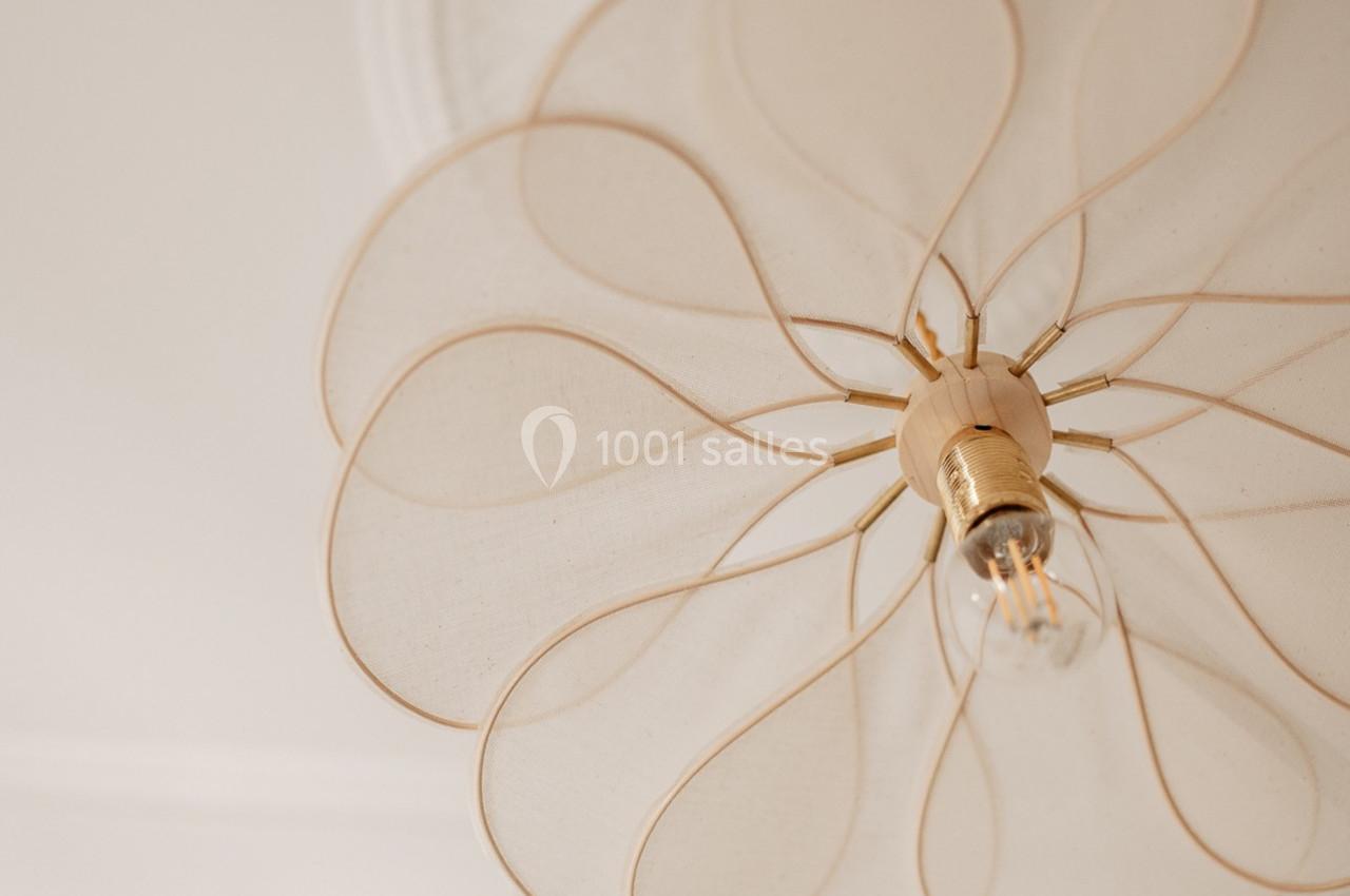 Suspension lumineuse en tissu beige clair avec une ampoule visible, vue en contre-plongée.