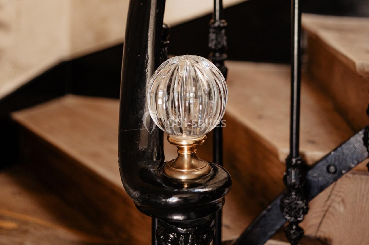 Pommeau d'escalier en verre transparent monté sur une base en laiton, fixé à une rampe en métal noir.