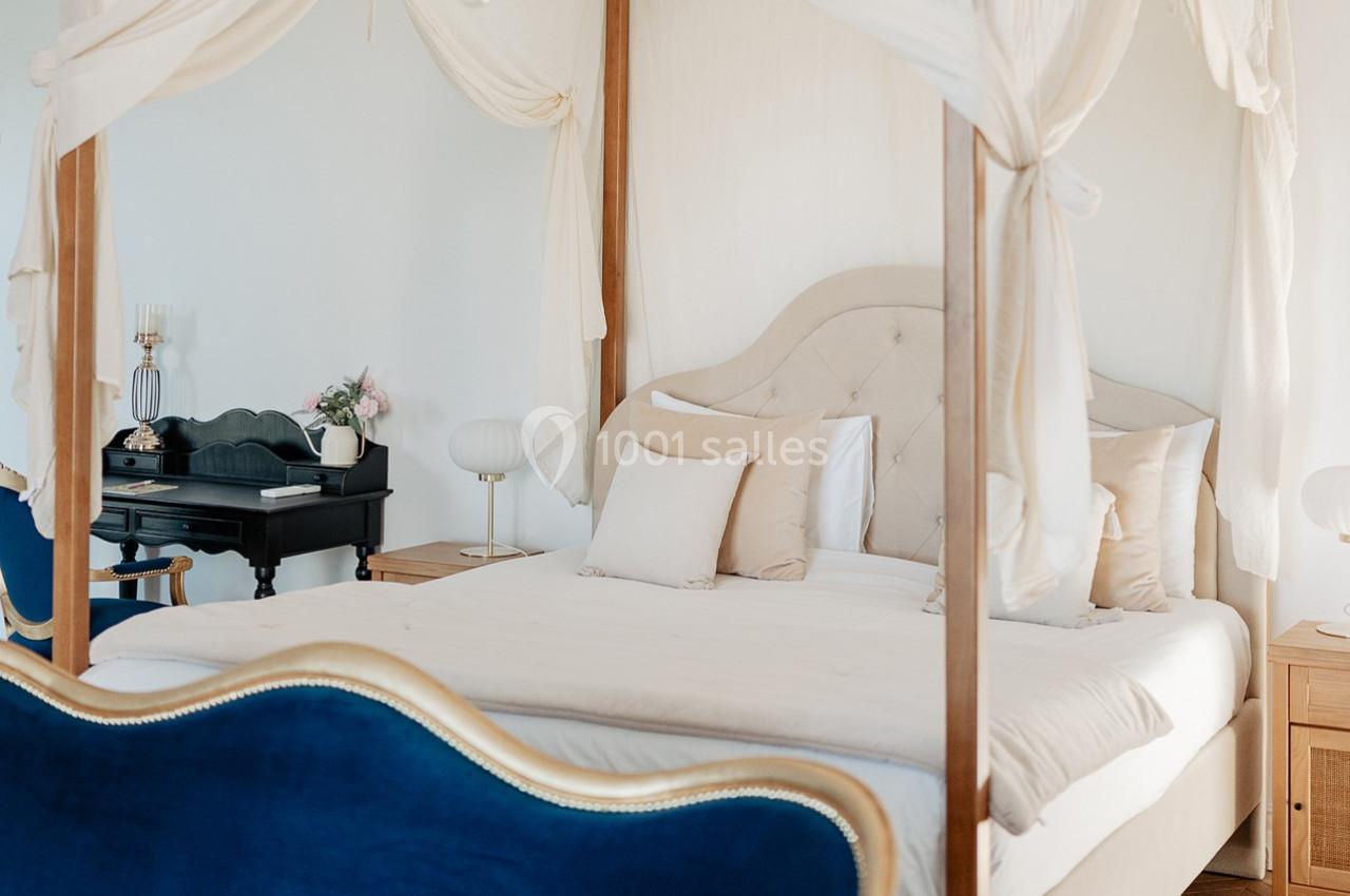 Lit à baldaquin avec drapés blancs dans une chambre lumineuse, décorée de meubles élégants et d'un bureau noir.