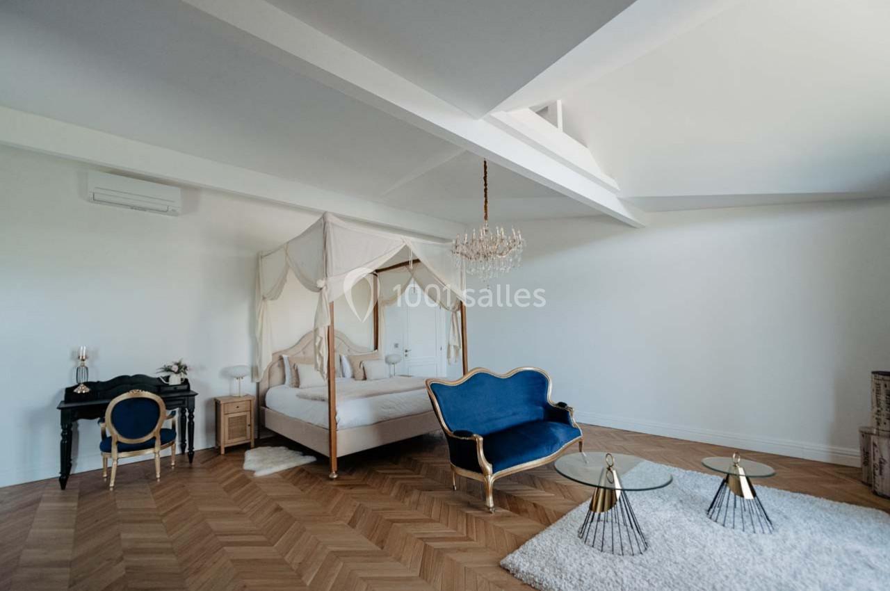 Chambre lumineuse avec lit à baldaquin, canapé bleu, parquet en bois et décoration élégante.