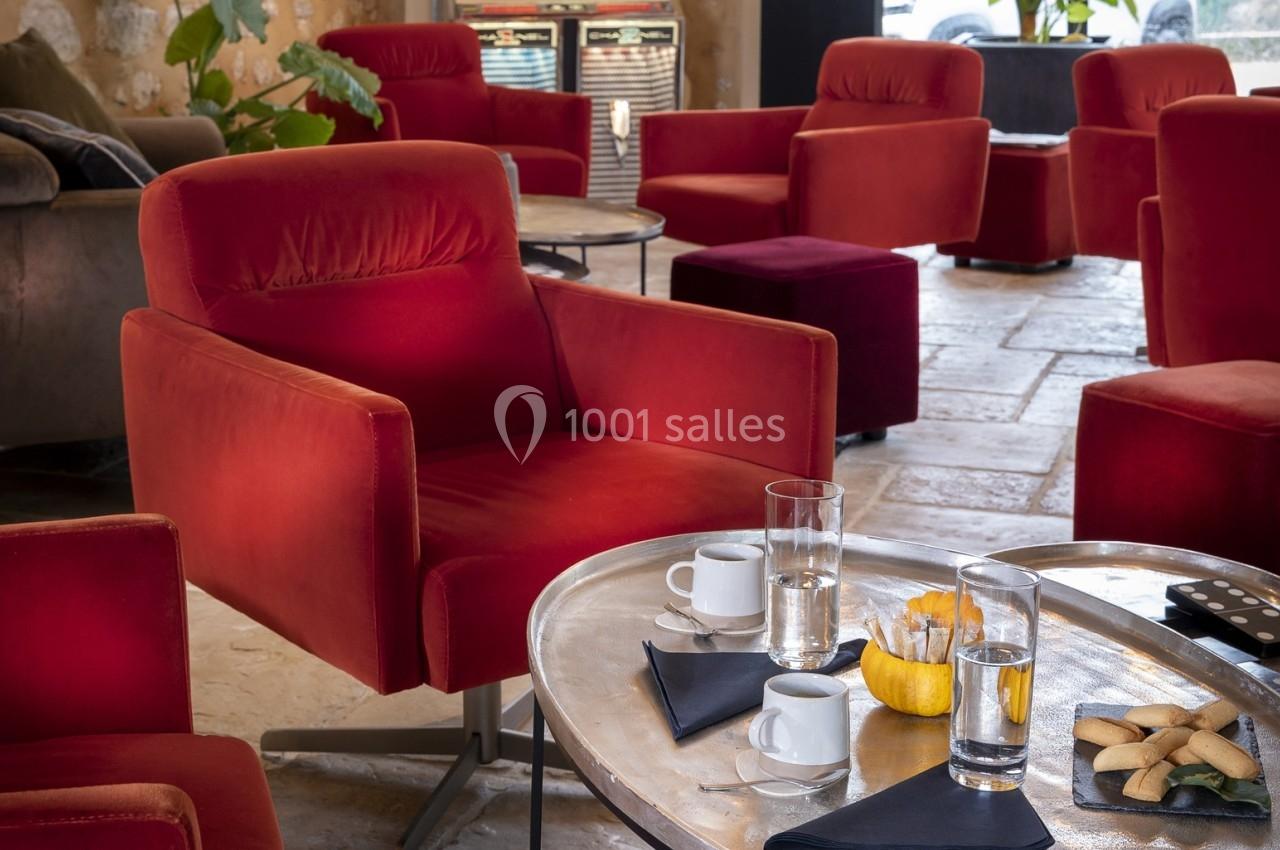 Fauteuils rouges dans un salon avec table basse en métal, verres, tasses de café, biscuits et serviettes noires.