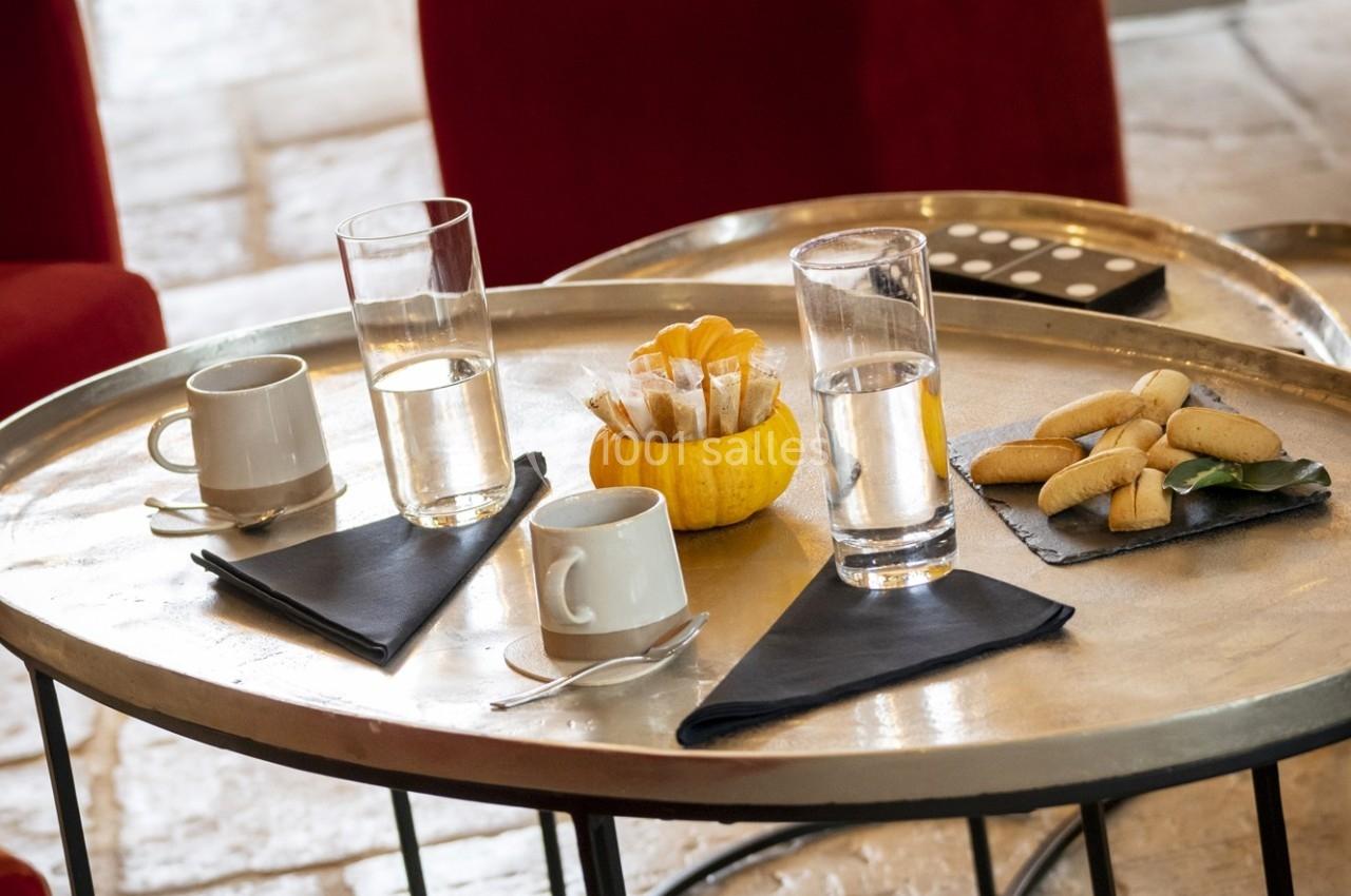 Table ronde avec tasses, verres d'eau, madeleines sur ardoise et pot décoratif en forme de citrouille.