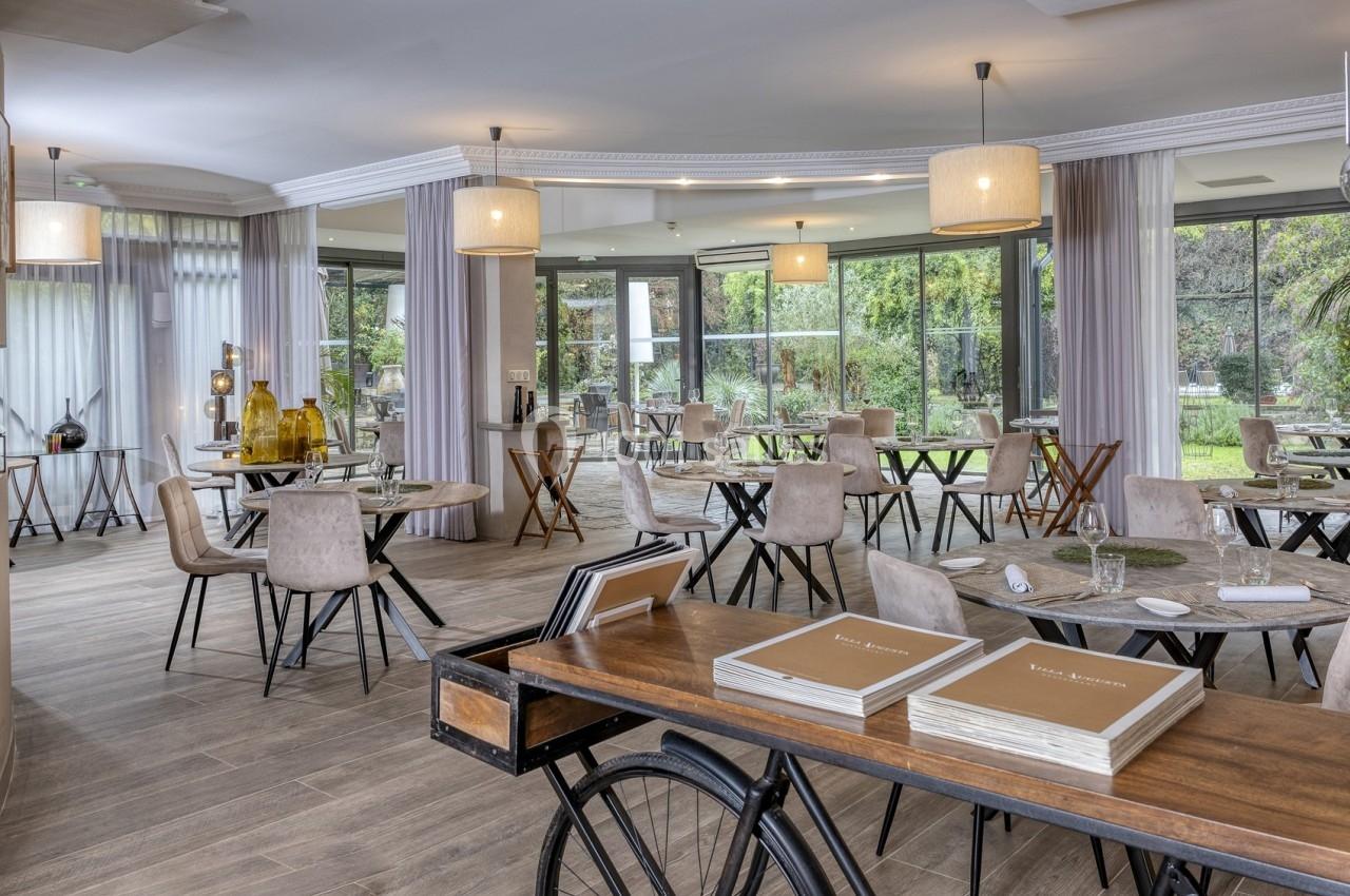 Salle de restaurant lumineuse avec grandes baies vitrées, tables espacées et décoration moderne.
