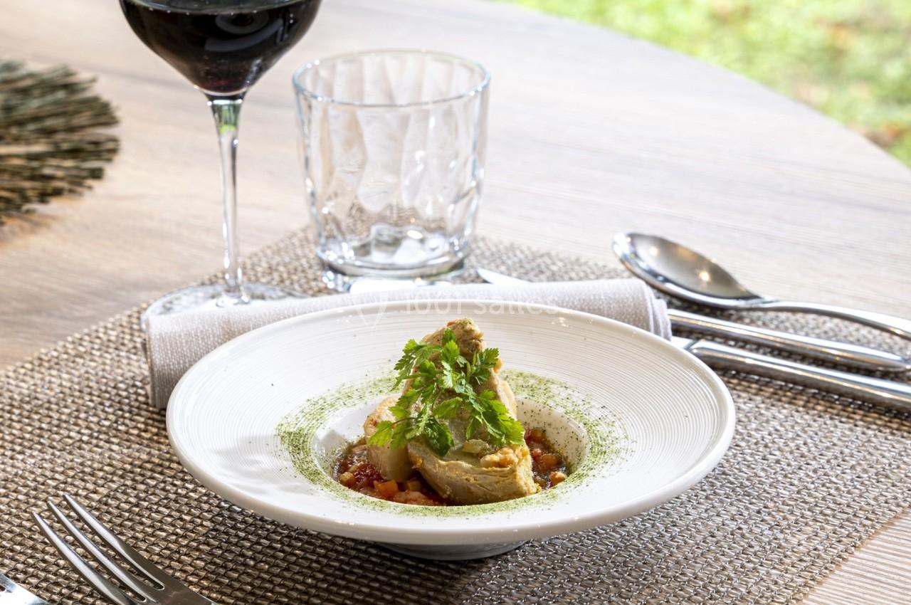 Assiette de plat gastronomique avec légumes et herbes, servie sur une table dressée avec verre de vin et couverts.