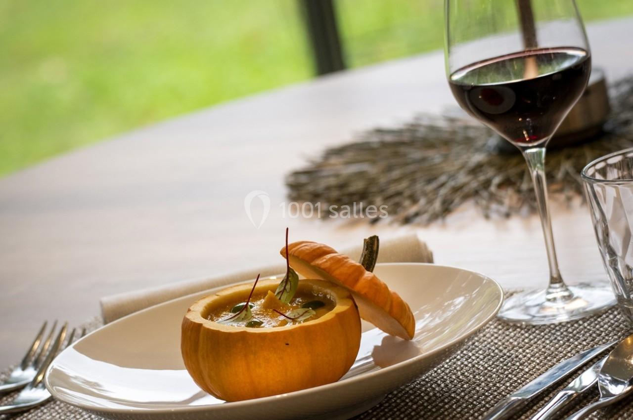 Une soupe servie dans une petite citrouille, accompagnée d'un verre de vin rouge sur une table dressée.