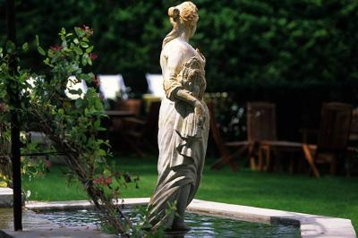 Statue en pierre représentant une femme tenant des épis de blé, placée au centre d'un bassin dans un jardin verdoyant.