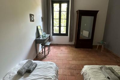 Chambre lumineuse avec deux lits simples, un bureau, une armoire en bois et une fenêtre donnant sur un jardin.