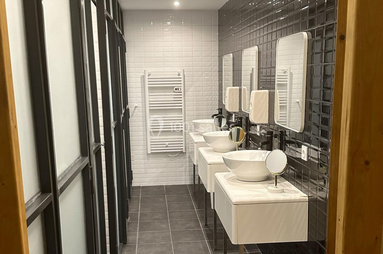 Salle de bain moderne avec trois lavabos, miroirs, carrelage noir et blanc, et un sèche-serviettes mural.