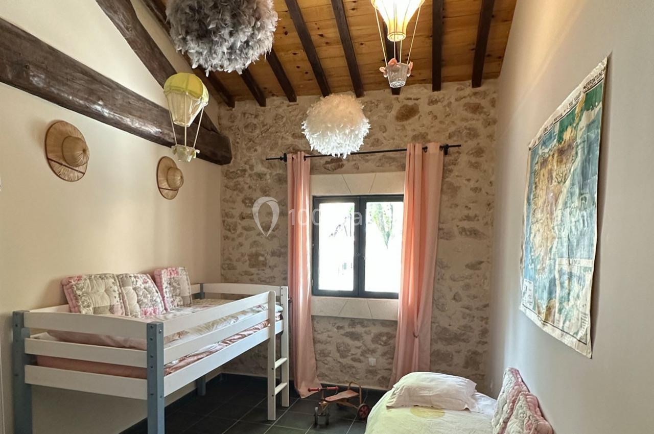 Chambre avec lits superposés, murs en pierre, plafond en bois, décorations aériennes et lumière naturelle.