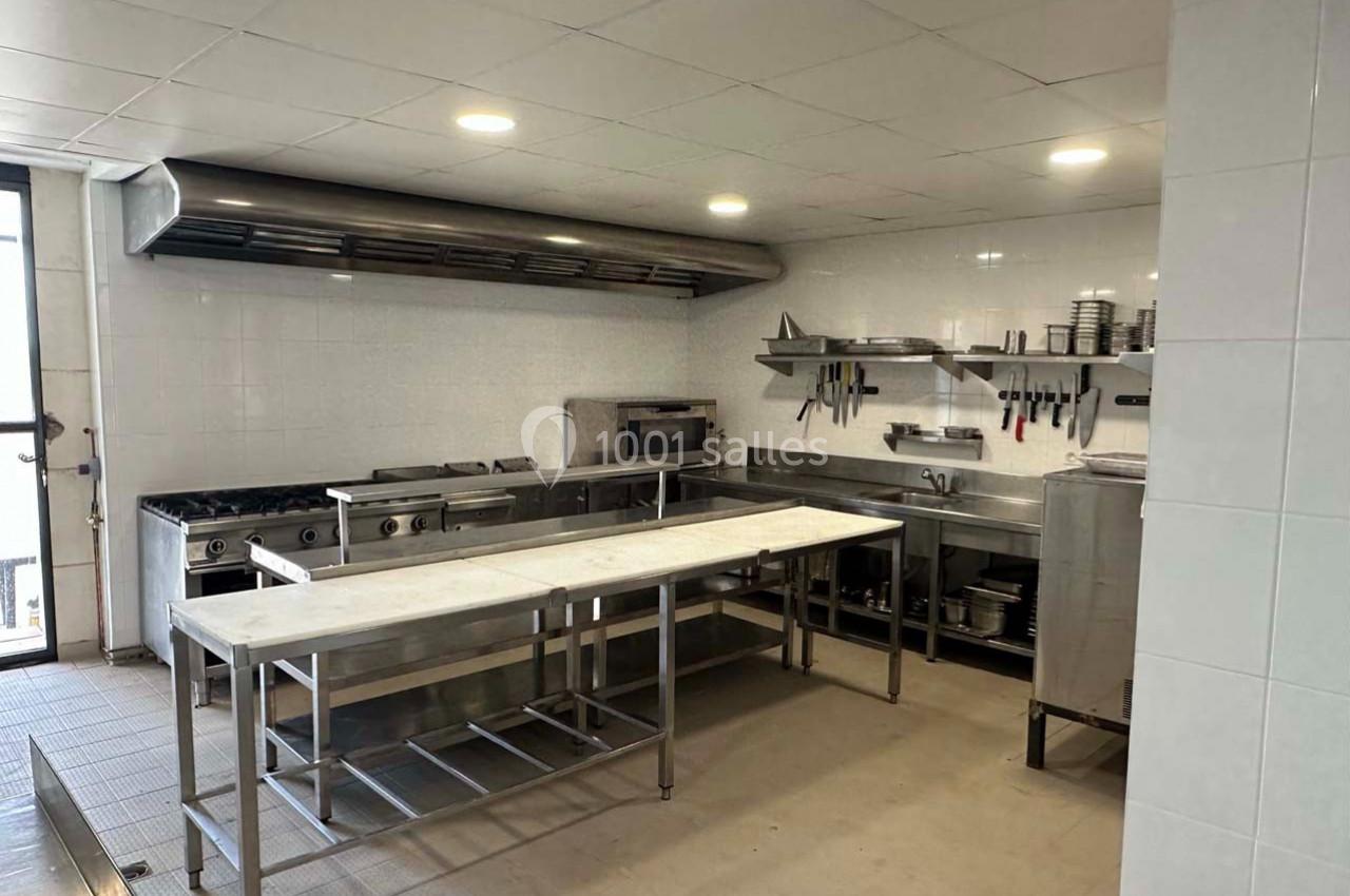 Cuisine professionnelle avec plan de travail en inox, équipements de cuisson, étagères et ustensiles accrochés au mur.