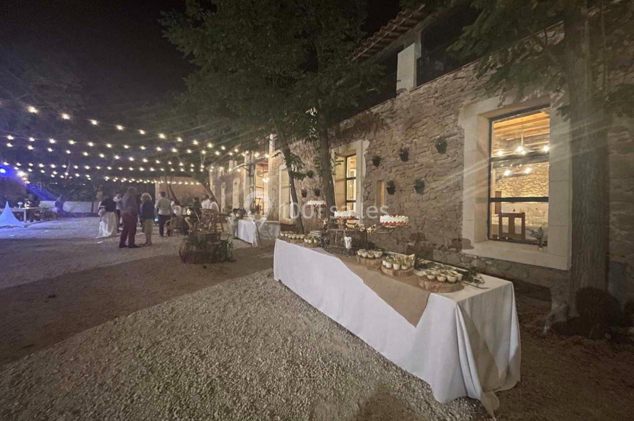 Table de buffet dressée en extérieur sous des guirlandes lumineuses, près d'un bâtiment en pierre, de nuit.