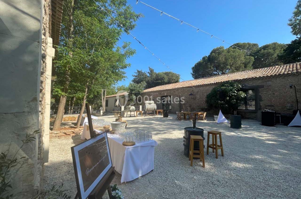 Cour extérieure ensoleillée avec tables, chaises et décorations pour un événement, entourée de bâtiments en pierre et d…