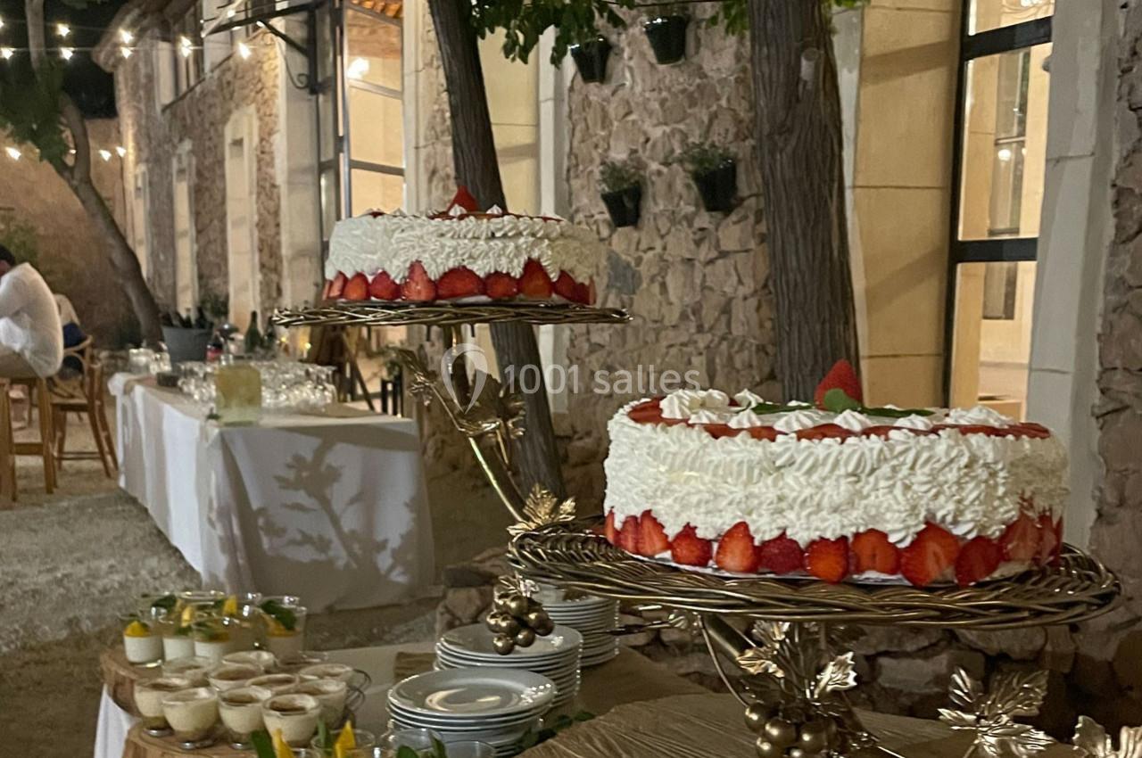 Deux gâteaux décorés de fraises et de crème sur des présentoirs dorés, entourés de desserts et d'une table dressée en…