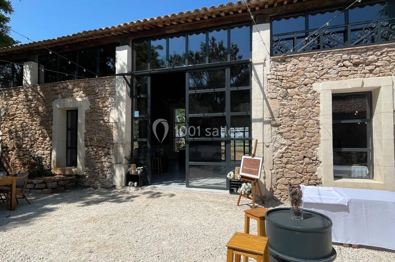 Façade en pierre d'un bâtiment avec de grandes baies vitrées, entouré d'une cour en gravier et de mobilier extérieur.