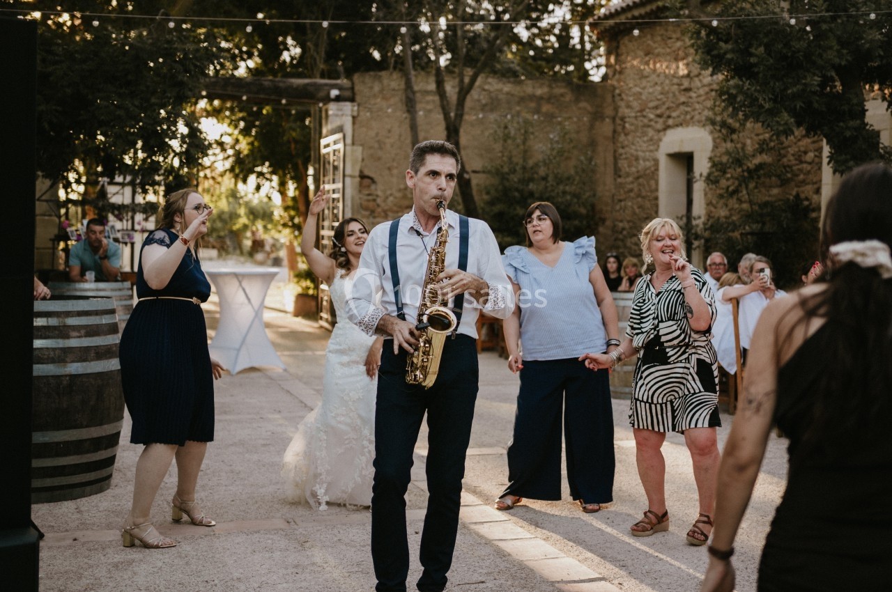 Un musicien jouant du saxophone mène un groupe de personnes dansant en extérieur lors d'une fête.