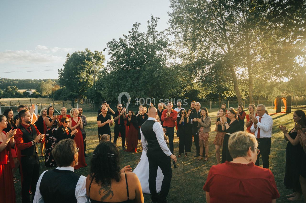 Un couple de mariés danse au centre d'un groupe de personnes applaudissant dans un jardin ensoleillé.