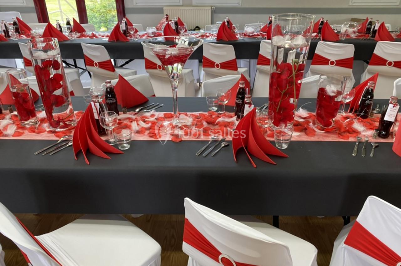 Salle décorée pour un événement avec tables noires, nappes rouges et blanches, pétales et centres de table fleuris.