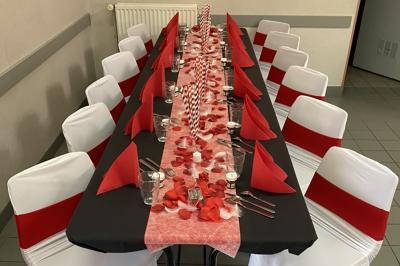 Salle décorée pour un événement avec des tables dressées en noir, rouge et blanc, et des chaises assorties.