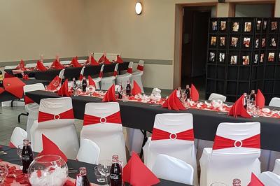 Salle décorée pour un événement avec des tables dressées en noir, rouge et blanc, et des chaises assorties.