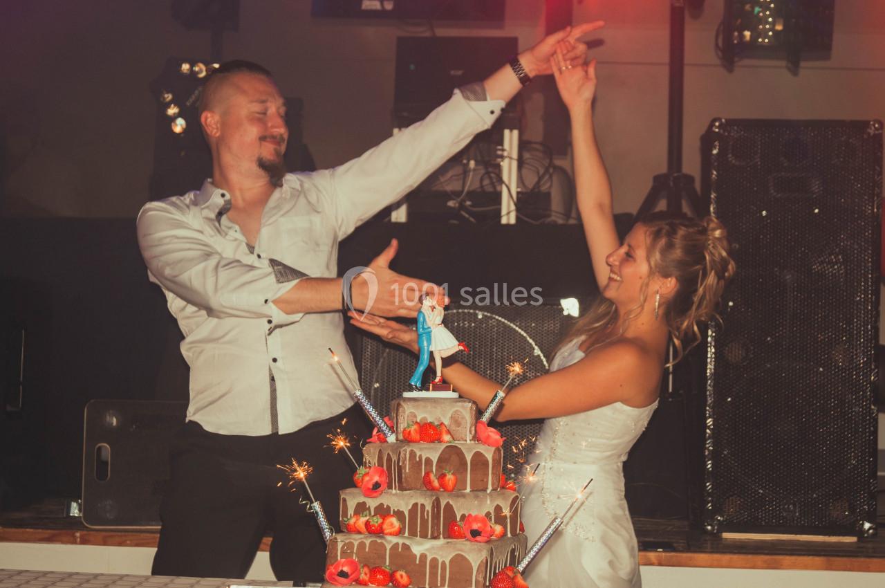 Un couple danse joyeusement devant un gâteau de mariage décoré de fleurs et de figurines, avec des étincelles allumées.