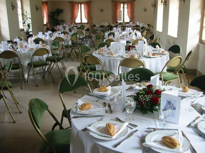 Salle de réception avec des tables rondes dressées, nappes blanches, chaises pliantes vertes et décorations florales.