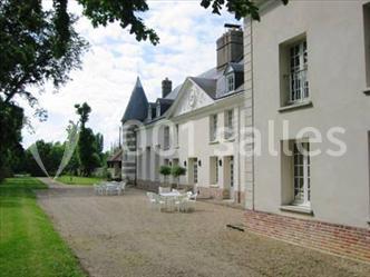 Façade d'un bâtiment ancien avec des murs clairs, des fenêtres à volets et une terrasse avec des tables et chaises.