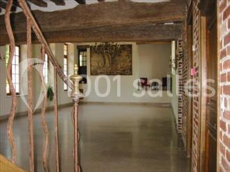 Intérieur d'une pièce lumineuse avec poutres en bois, murs en briques, sol en pierre et escalier en fer forgé.