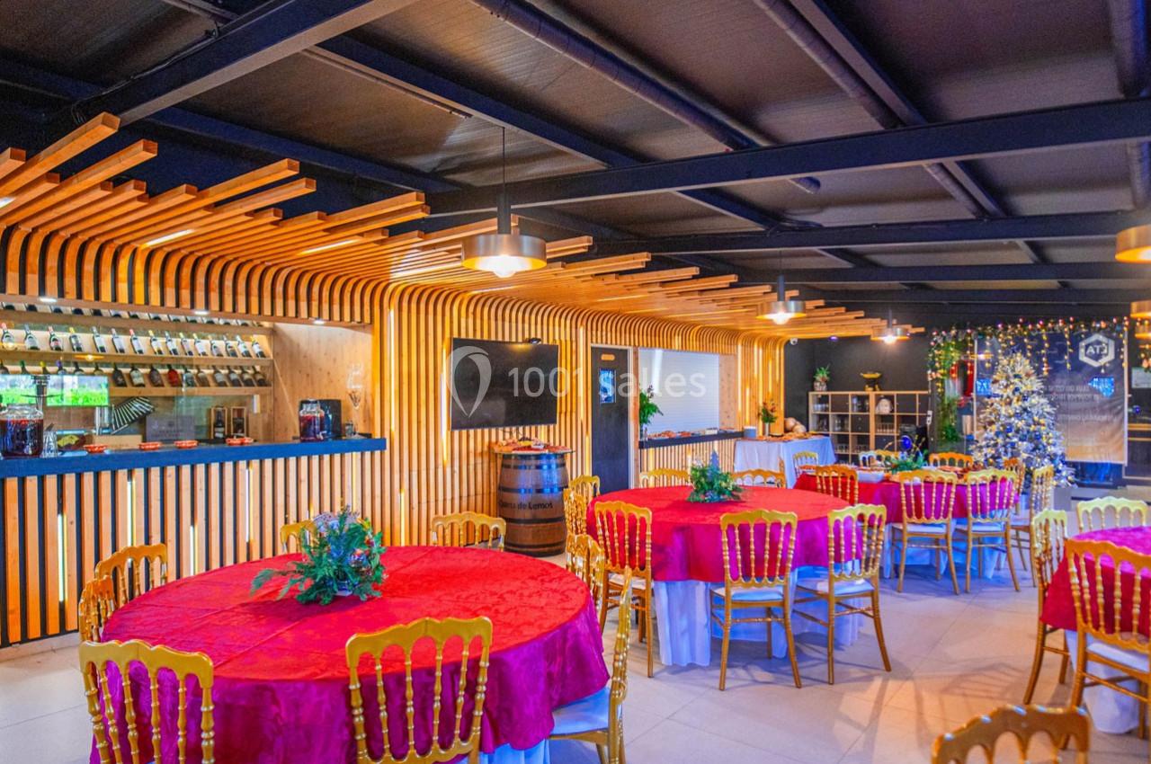 Salle de réception décorée avec des tables rondes nappées de rouge, chaises dorées et éclairage chaleureux.