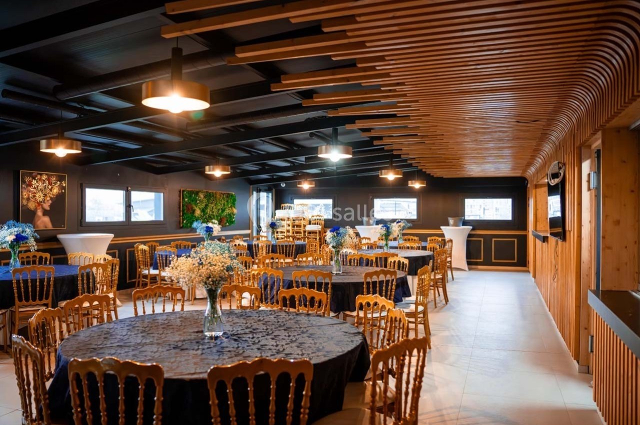 Salle élégante avec tables rondes décorées de nappes bleues et bouquets, éclairée par des suspensions modernes.