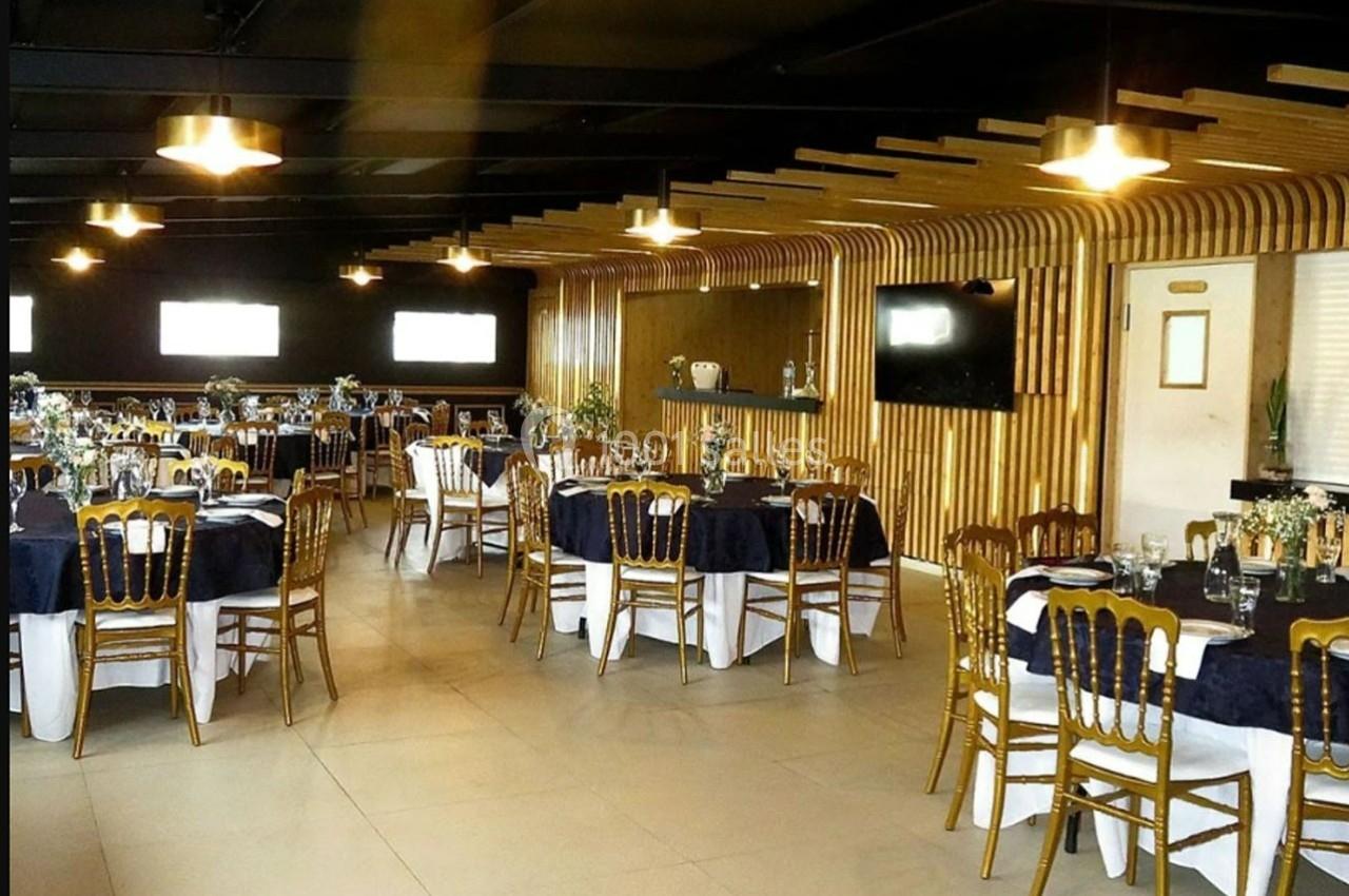 Salle de réception élégante avec tables dressées, chaises dorées et décoration en bois moderne.