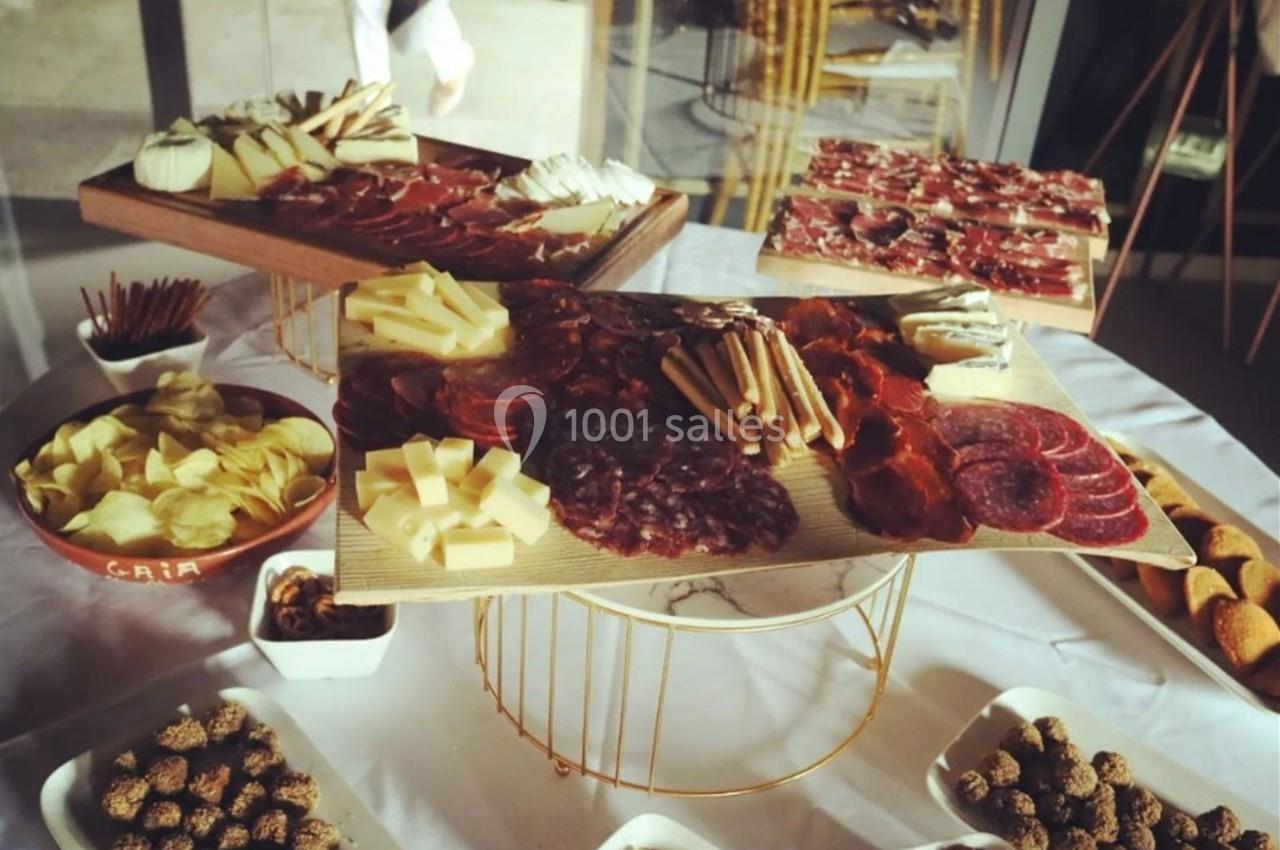 Plateaux de charcuterie et fromages variés entourés de bols de chips, fruits secs et autres accompagnements sur une table.