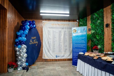 Décoration d'anniversaire avec ballons bleus, table de buffet garnie et panneaux d'information dans une salle en bois.