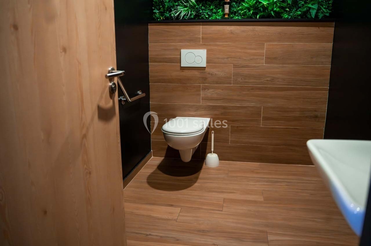 Toilettes modernes avec cuvette suspendue, murs et sol en bois, et décoration végétale en arrière-plan.