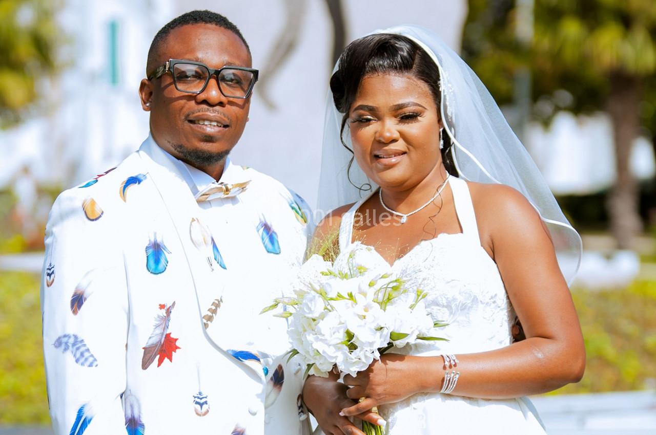 Un couple en tenue de mariage pose ensemble, la mariée tenant un bouquet de fleurs blanches.