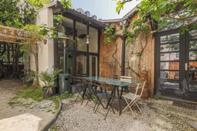 Balcon étroit avec sol en bois, mur en pierre, grillage métallique et vue sur un jardin arboré.