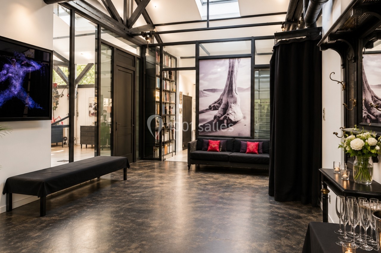 Espace intérieur moderne avec sol en bois sombre, canapés noirs, grandes photos murales et décoration élégante.