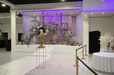 Salle de réception décorée avec des chaises blanches alignées et des arrangements floraux, prête pour un événement.