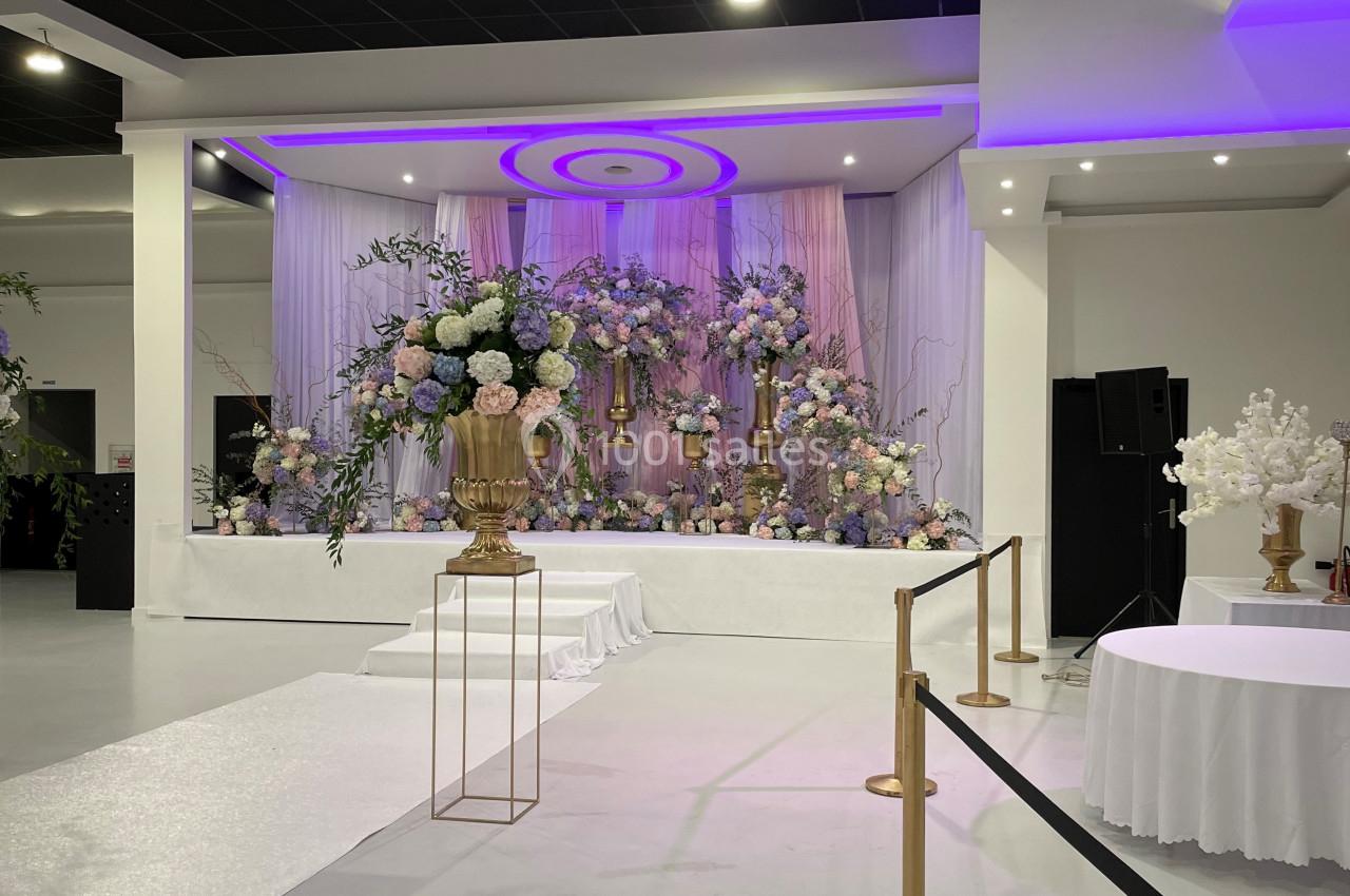 Décoration florale élégante avec des fleurs pastel sur une scène dans une salle de réception moderne et lumineuse.