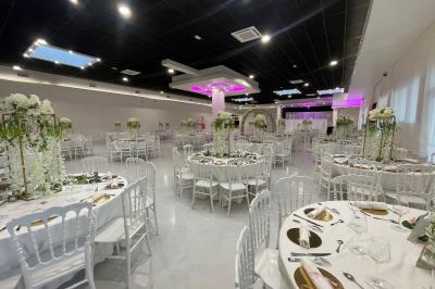 Salle de réception décorée avec des chaises blanches alignées et des arrangements floraux, prête pour un événement.