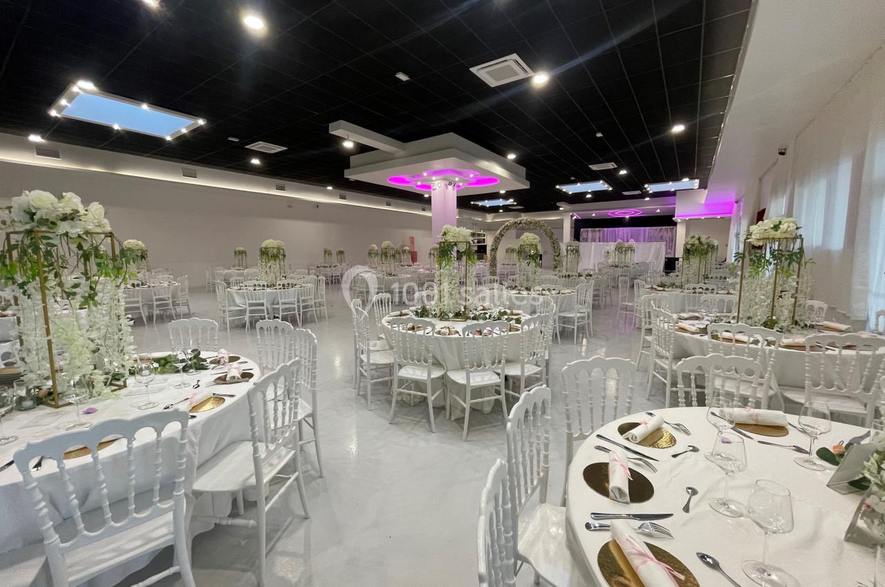 Salle de réception élégamment décorée avec des tables rondes, des chaises blanches et des arrangements floraux.