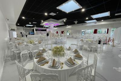 Salle de réception décorée avec des chaises blanches alignées et des arrangements floraux, prête pour un événement.